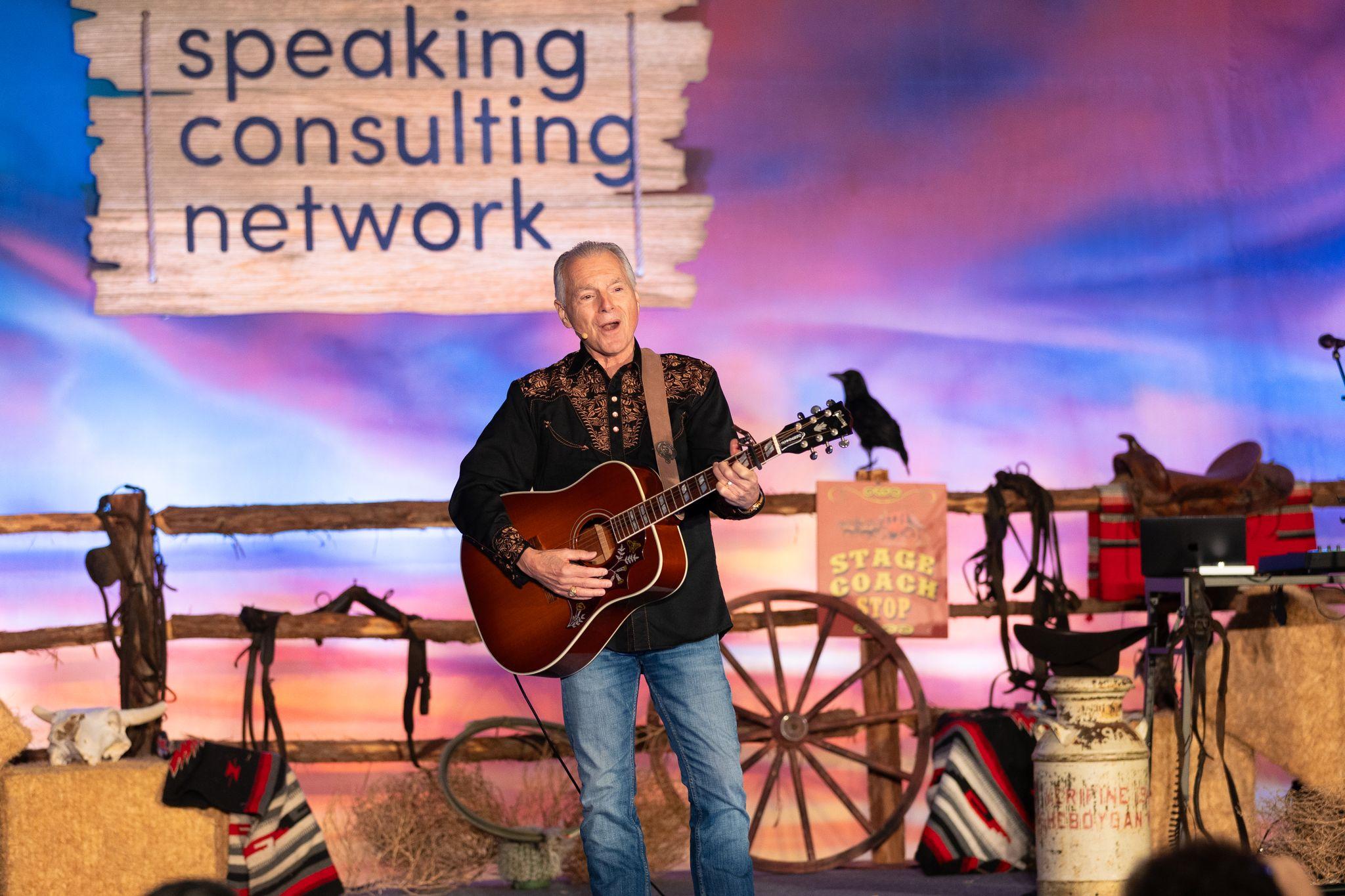 Jim Cathcart performing live with guitar on stage at Speaking Consulting Network