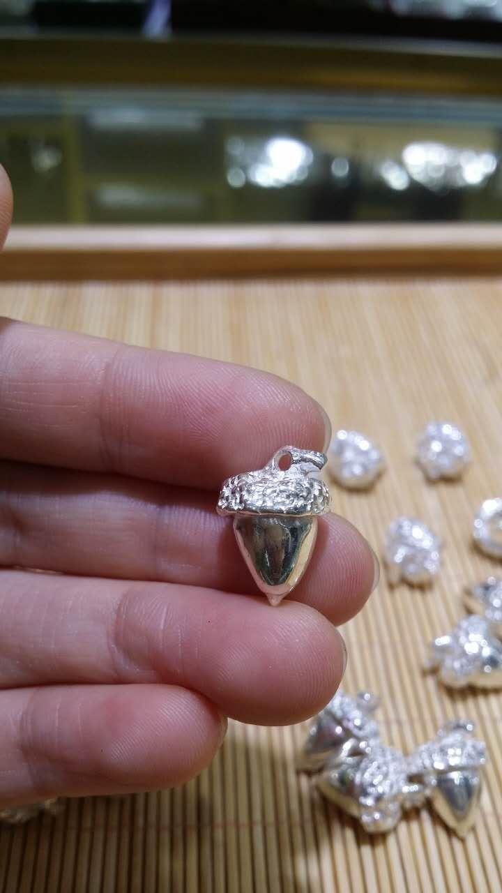 Silver acorn charm held between Jim's fingers, showing detail of the craftsmanship